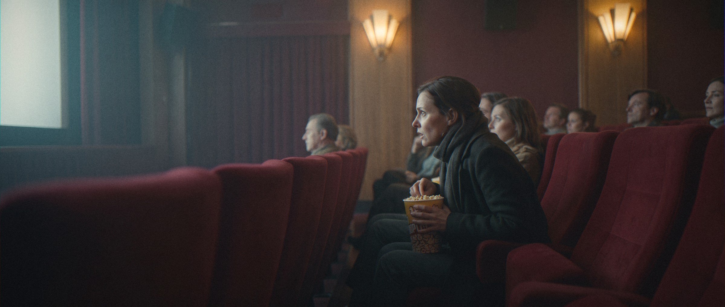 In een klassieke bioscoopzaal met rode stoelen leunt een vrouw gegrepen naar voren terwijl de film begint