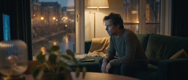 Laat op de avond zit een man voorovergebogen op de bank, gegrepen door de serie die hij kijkt