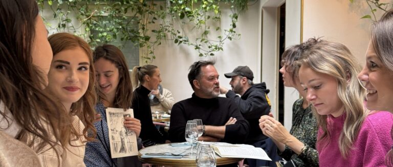 Deelnemers aan de werkreis in Parijs zitten samen aan tafel in een lichte kas met groen en zijn met elkaar in gesprek