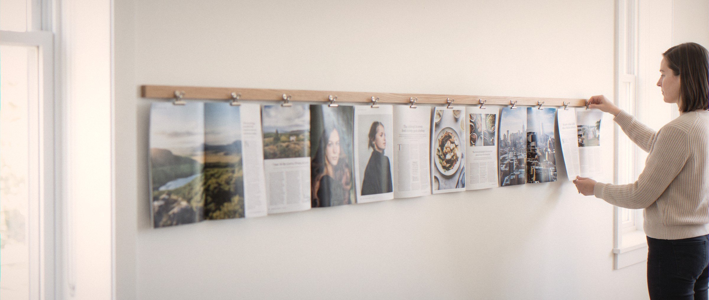 Een redacteur schuift een pagina onder een houten lijst, waar één rij pagina's van een nummer op volgorde hangt